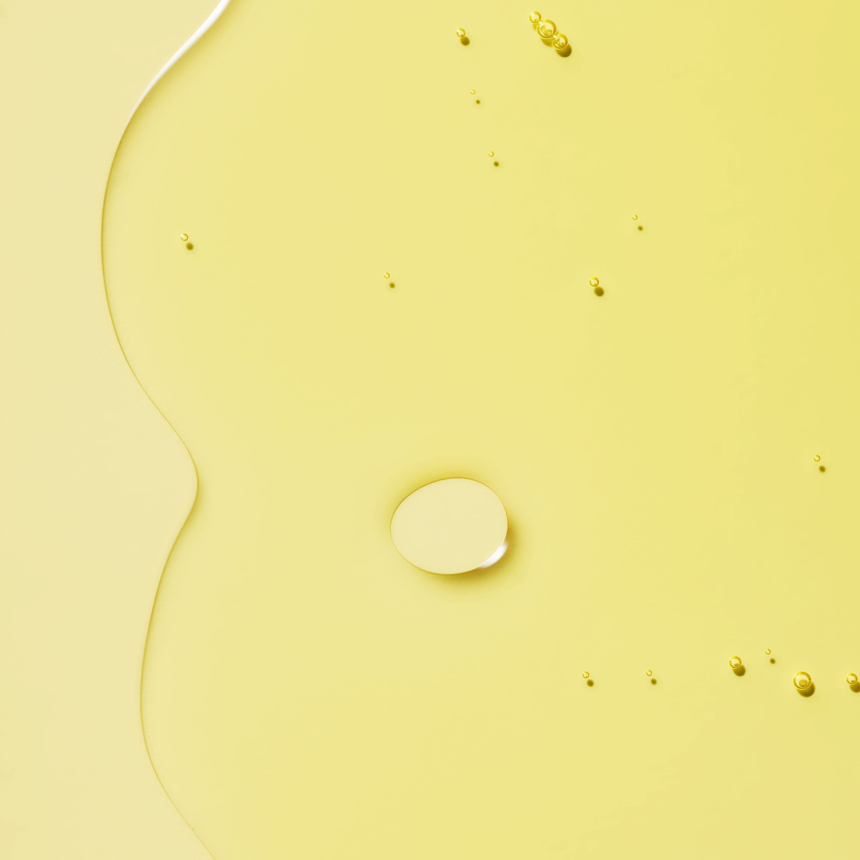 A smooth oil with droplets dispersed on a yellow background.