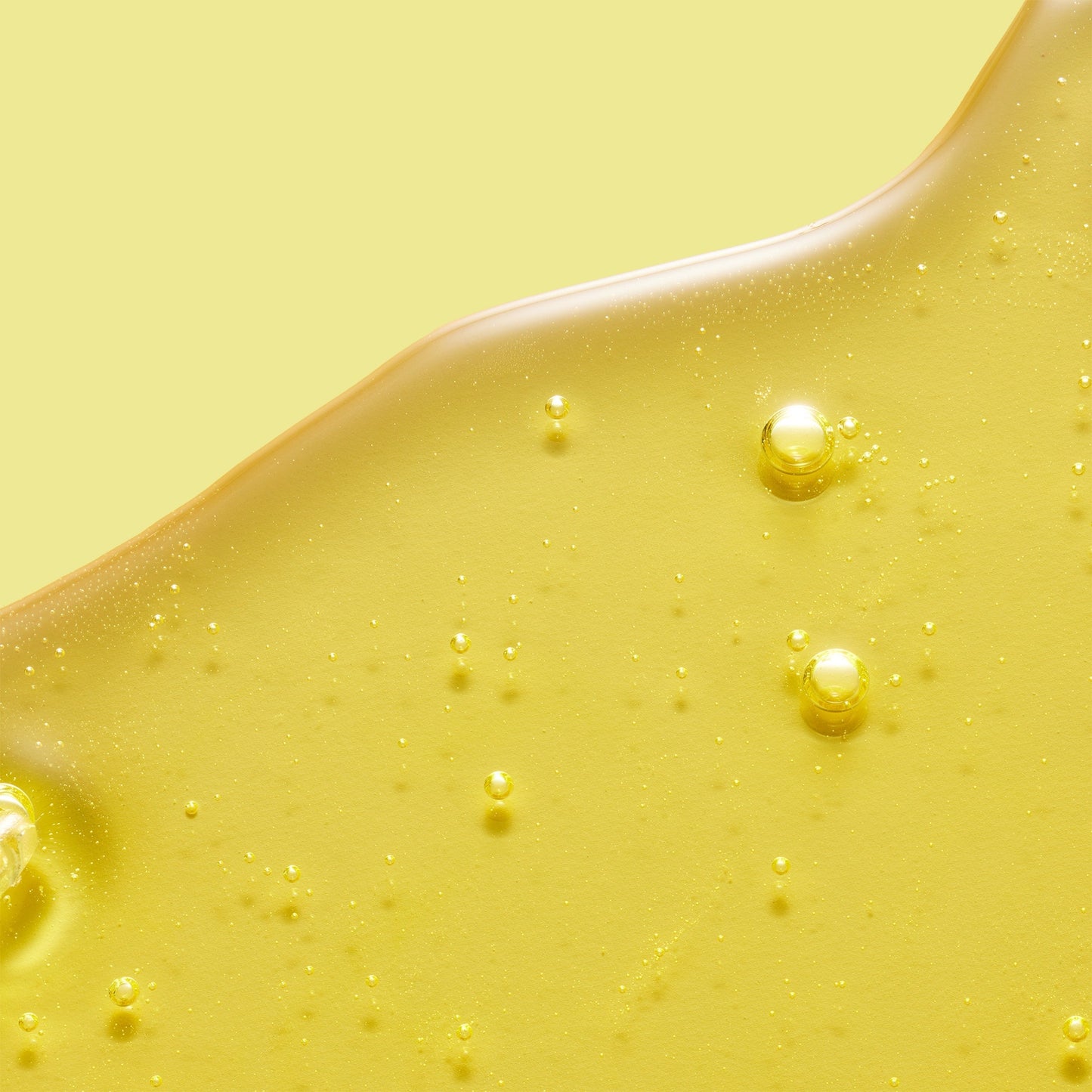 A yellow gel-like skincare product with bubbles, set against a matching yellow background.