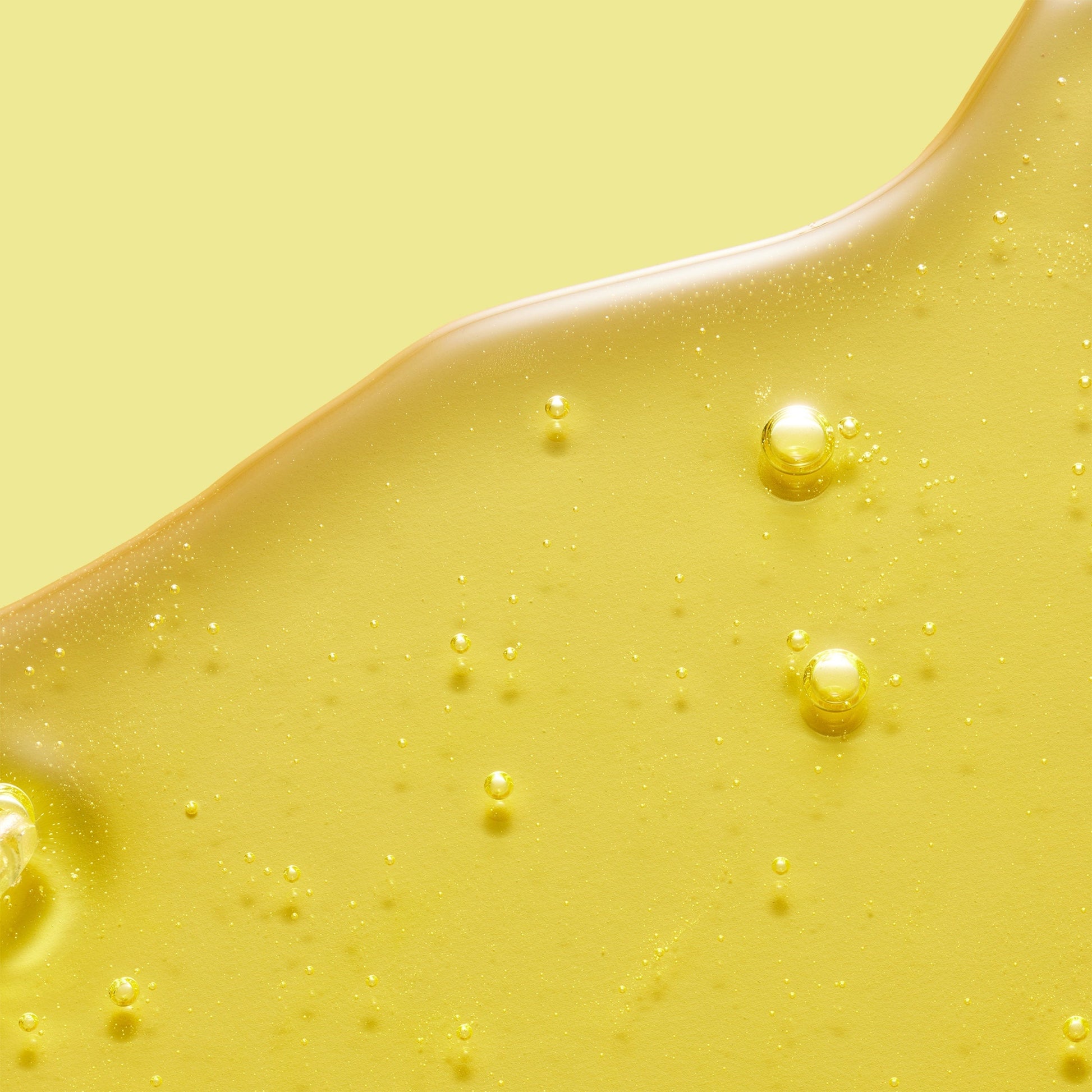 A yellow gel-like skincare product with bubbles, set against a matching yellow background.