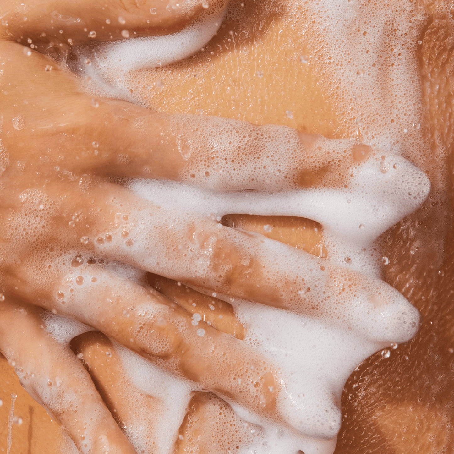 Close up of a hand lathering product on skin with lots of suds.