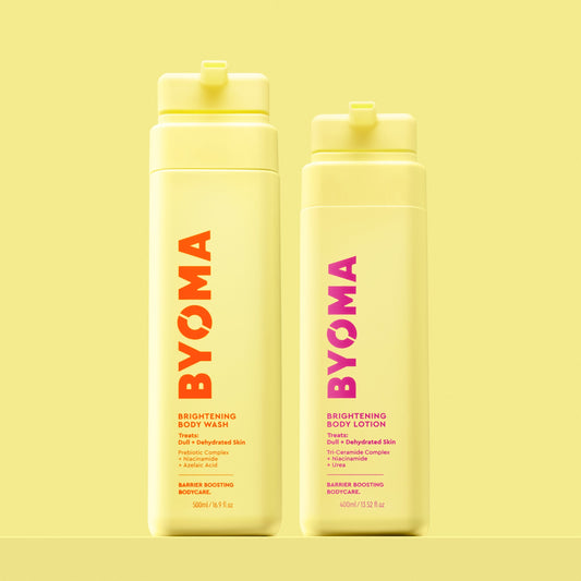 Two yellow BYOMA bottles on a pastel yellow background. Left: Brightening Body Wash with orange-red text; right: Brightening Body Lotion with pink text. Both are upright.