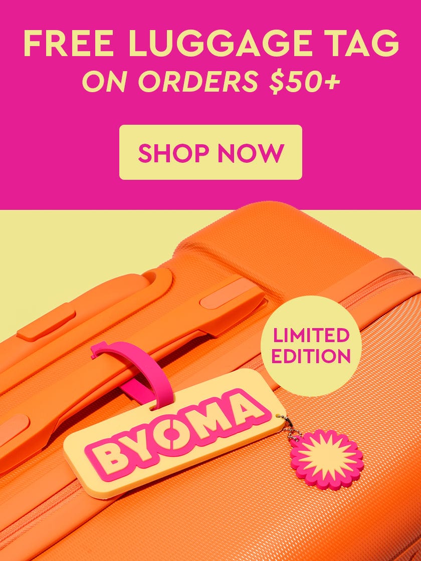 Orange suitcase with a BYOMA luggage tag on a pink background text "Free Luggage Tag On Orders Over $50. Shop Now"
