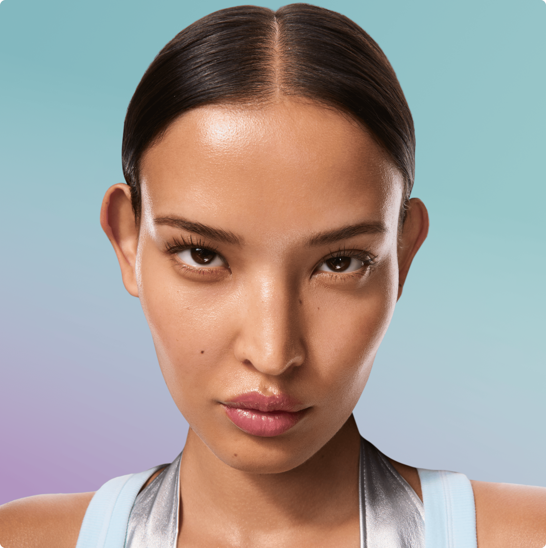 A close-up portrait of a woman with slicked-back dark hair and a neutral expression, wearing a light blue and silver athletic top against a soft blue-to-purple gradient background.