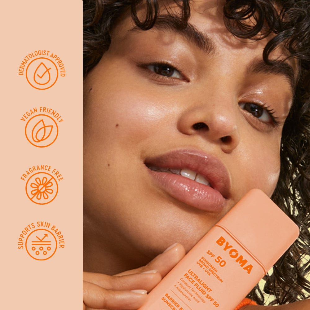 Woman holding a Byoma sunscreen bottle with product features on the side.