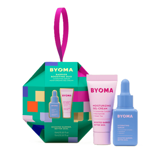 A green, multi-colored ornament-shaped gift box labeled “BYOMA Barrier Boosting Duo,” featuring a pink tube of moisturizing gel-cream and a blue bottle of hydrating serum.   The background is transparent.
