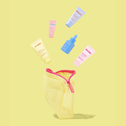 A yellow zippered mesh pouch is open at the bottom of the image, with five miniature BYOMA skincare products floating out above it in an arc. The background is pastel yellow.